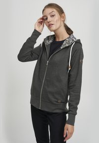 Felpa grigia con zip, con fodera del cappuccio a motivo floreale, coulisse con dettagli in legno e una toppa con il logo sul maniche sinistra.
