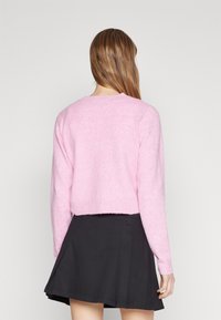 Rosa, mjuk, kortärmad tröja med lång ärm och rund halsringning, matchad med en svart kjol. Texturen ser ludden och lätt ut.