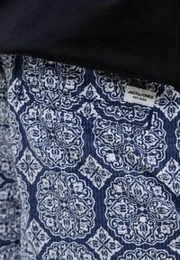 Tessuto blu con motivo a fiori bianchi. L'etichetta visibile riporta "JACK & JONES EST.1990." Texture liscia; materiale leggero e casual.