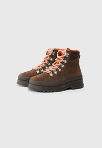 Botas de senderismo de ante marrón con cordones naranjas, herrajes de ojales de metal, suela texturizada y cuello acolchado para mayor soporte. Diseño robusto y duradero.