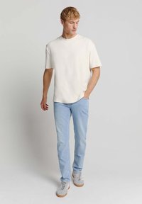 Witte korte mouwen t-shirt, lichtblauwe jeans en grijze sneakers. Casual pasvorm met een ronde halslijn en klassieke denimstijl.