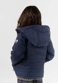 Giubbotto puffer blu navale con cappuccio, dotato di un dettaglio in gomma con logo sul retro, tasche con zip e materiale testurizzato.