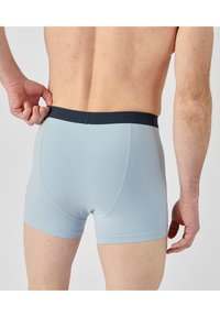 Boxer shorts azzurri chiari realizzati in tessuto elasticizzato, con un cinturino di colore blu navy e un design aderente caratterizzato da una texture liscia.