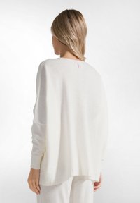 Witte oversized trui van zacht materiaal, met een ronde halslijn en iets verlaagde schouders. Opvallend labeldetail aan de achterkant.