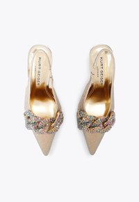 Beżowe szpilki slingback z wydłużonym noskiem i iryzującą teksturą, ozdobione wielokolorowym koralikowym łańcuchem z przodu. Złote logo na wkładce.