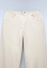 Beige cotton pants with a smooth texture, featuring front pockets, a button closure, and belt loops. No visible patterns or accents.