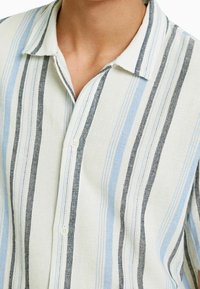 Camisa a rayas hecha de tejido ligero, con líneas verticales en azul claro, azul marino y crema, con un cuello clásico y cierre de botones.