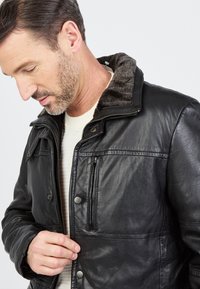 Zwarte leren jas met een zachte, grijze, bontvoering col, rits- en drukknoopsluitingen, en voorzakken. Soepele textuur en op maat gemaakte pasvorm.