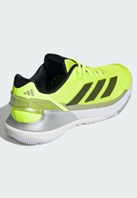 Neon yellow athletic shoe featuring a mesh upper, black accents, reflective silver heel, and a textured rubber sole. Lightweight design.