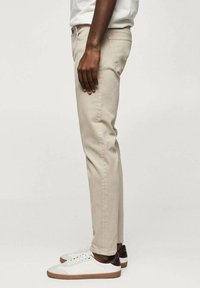 Pantalones de algodón beige con un ajuste slim, que cuentan con bolsillos frontales y cierre de botón, combinados con zapatillas blancas y marrones.