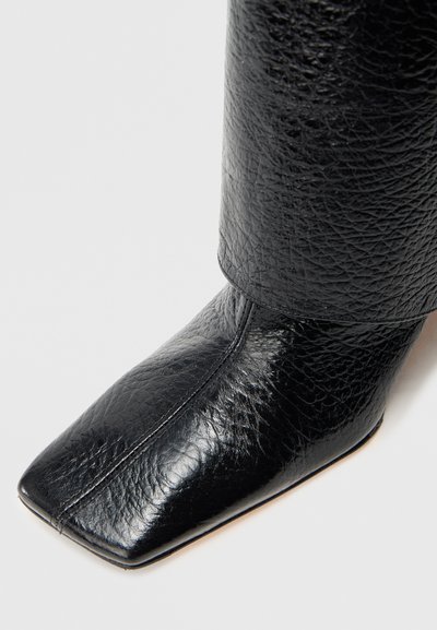 Čierna kožená členková čižma so štvorcovou špičkou, štruktúrovaným povrchom a elegantným profilom. Výrazné švy pozdĺž nártu.