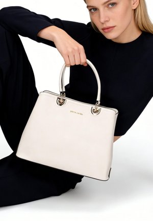 Donna con abito nero che tiene una borsa bianca Pierre Cardin con doppi manici su sfondo semplice.