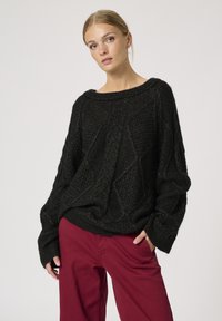 Sort strikket sweater med løs pasform, strukturerede diamantmønstre, bred halsudskæring og ribbede manchetter, parret med bordeauxfarvede bukser.