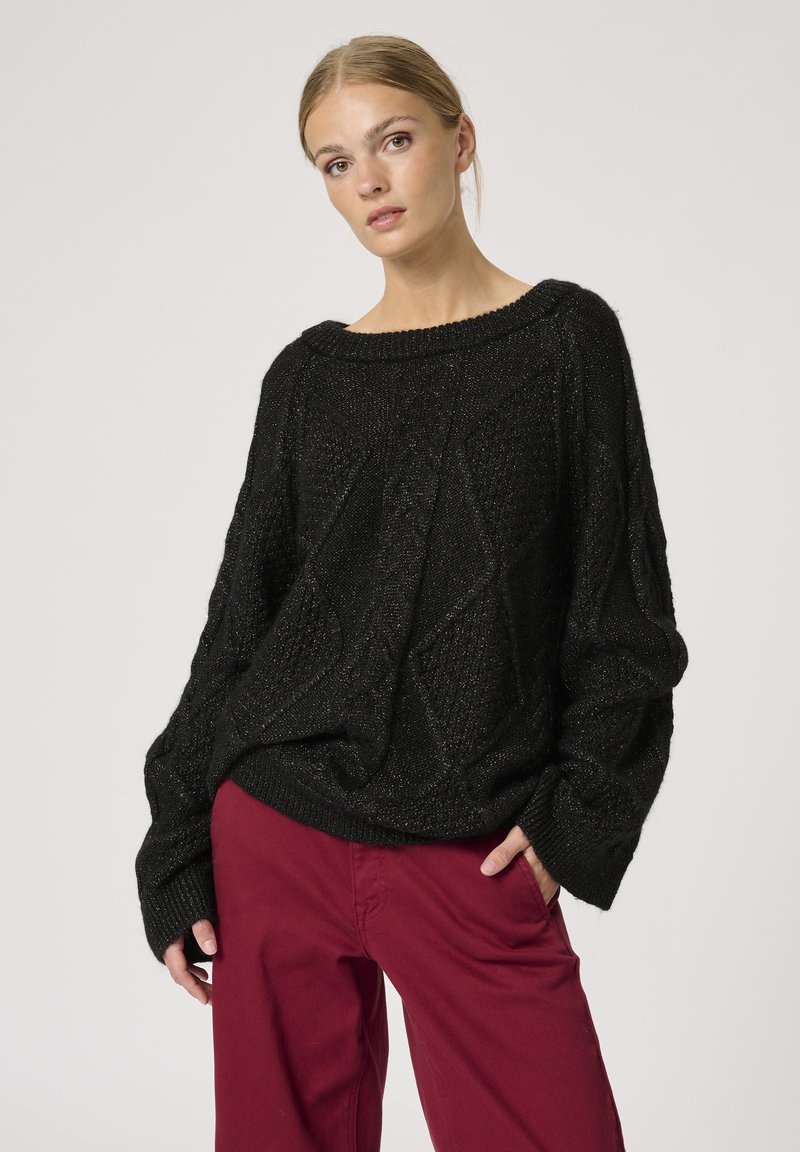 Sort strikket sweater med løs pasform, strukturerede diamantmønstre, bred halsudskæring og ribbede manchetter, parret med bordeauxfarvede bukser.