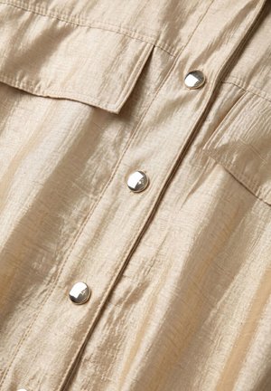 Beige crinkled fabric with two flap pockets and four shiny round silver buttons down the center front of a garment.