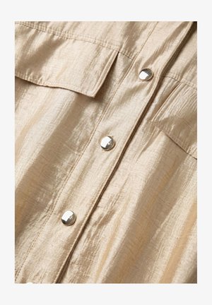 Beige crinkled fabric with two flap pockets and four shiny round silver buttons down the center front of a garment.