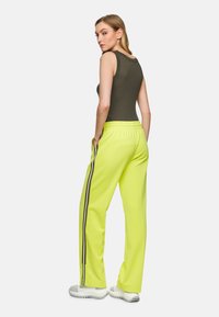 High-waisted neon yellow track pants with black side stripes, made of lightweight material, paired with a fitted dark tank top.