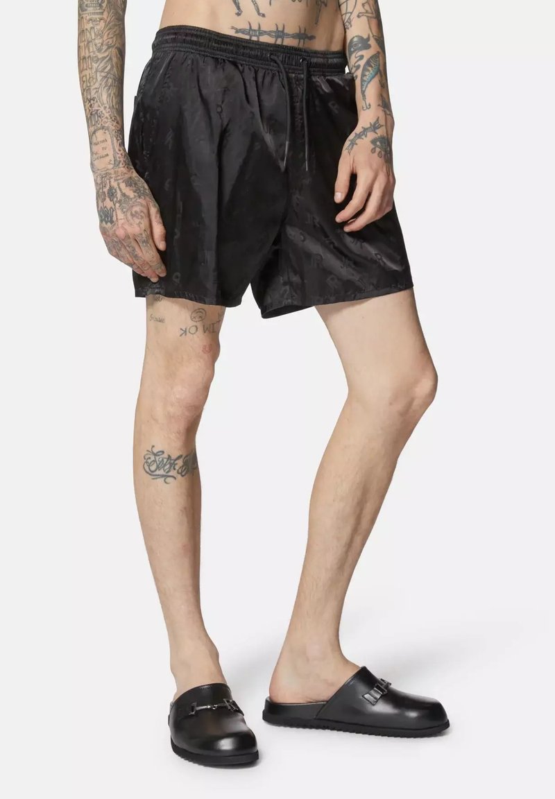 Bermudas de natation noires avec un motif subtil, taille élastique et poches latérales, accompagnées de sandales noires à glisser avec une bride décorative.