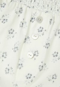 Witte stof met grijs bloemendessin, voorzien van een smocktaille en een drieknopenpat met ronde, witte knopen.