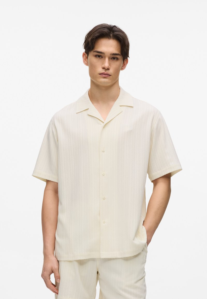 Chemise à manches courtes avec boutons, couleur crème clair à fines rayures verticales, texture douce, coupe décontractée et col cranté.