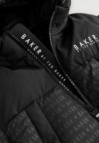 Crna пуховка sa ponovljenim uzorkom "Baker by Ted Baker" logotipa, s naglaskom na ovratniku i području zatvarača.