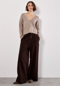Cárdigan de punto marrón claro con escote en V y botones, combinado con pantalones de pierna ancha marrón oscuro, que cuentan con bolsillos frontales y un corte relajado.