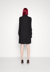 Robe en maille noire étincelante avec manches longues bouffantes, col montant et silhouette en ligne A, assortie à des chaussures à talons hauts noires.