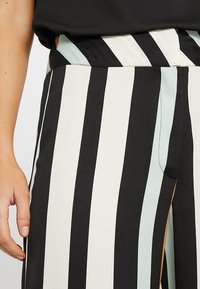 Pantalons rayés en noir et blanc contrastés avec des accents bleu clair et une texture de tissu lisse. Présente une taille ajustée et une couture sur le côté.