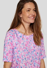 Lightweight top with a scoop neckline, featuring a pink and blue watercolor dot pattern; soft, textured fabric with short sleeves.