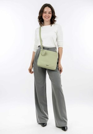 Light green leather crossbody bag with a smooth texture and heart-shaped accent. Features a long adjustable strap and a structured design.