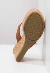 Platformové sandály s korkovou stélkou a gumovou podrážkou, s tkaným текстilním svrškem v teplé hnědé barvě a logem UGG na podrážce.