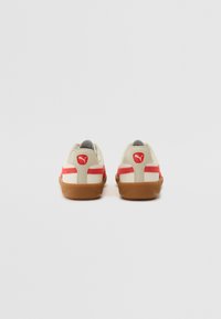 Sneakers Puma cu partea superioară crem, accente roșii și talpă din cauciuc din rasina. Caracteristici o parte din spate texturată și detaliu cu logo pe călcâi.