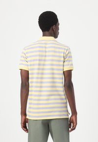 Chemise polo à rayures jaunes et lavande avec des manches courtes, un col, et des fentes sur les côtés de l'ourlet. Texture de tissu mate.