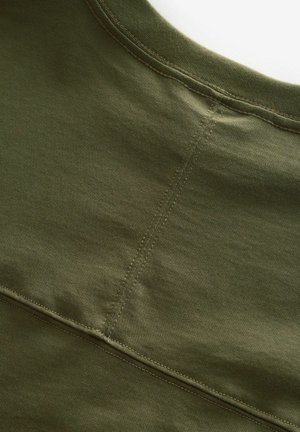 Camiseta de algodón verde oliva con escote redondo, que presenta costuras sutiles y una textura suave y lisa. Sin patrones ni accesorios visibles.