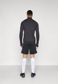 Αθλητική εμφάνιση με μαύρο εφαρμοστό μακρυμάνικο τοπ και μαύρο σορτς με λευκές πλευρικές ρίγες, συνδυασμένα με λευκές κάλτσες και μαύρα παπούτσια με τάπες.