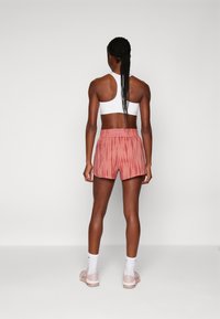 Idrettsantrekk bestående av en hvit sports-bh og rosa tie-dye shorts med elastisk liv. Modellen har på seg hvite sokker og lyse sko.