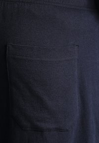 T-shirt bleu marine avec une texture douce, dotée d'une poche passepoilée. Le tissu présente une surface lisse et uniforme avec une légère élasticité.