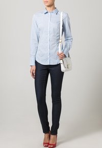 Ljust blått rutigt button-up skjorta kombinerat med mörka skinny jeans. Vit crossbody-väska och röda högklackade sandaler fulländar looken.