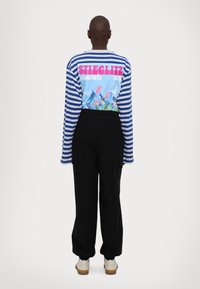 Μπλούζα μακρόμανικη ριγέ σε μπλε και γκρι, με πολύχρωμο γραφικό στο πίσω μέρος που περιλαμβάνει κείμενο. Συνδυασμένη με μαύρο φαρδύ παντελόνι.