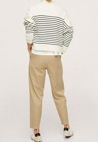Weiß-blau gestreifter Pullover, lockere Passform, mit aufgerollten Ärmeln; beiger, schmal zulaufender Hosen mit glatter Textur; weiße Sneakers mit schwarzen Akzenten.
