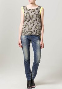 Top grigio a fantasia con maniche corte giallo neon, abbinato a jeans in denim sbiadito e tacchi aperti neri con dettagli a zip.