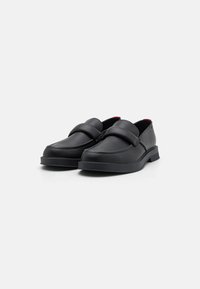 Chaussures en cuir noir avec une finition lisse, bout arrondi et une large sangle sur le cou-de-pied. Talon léger et accents intérieurs rouges.