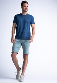 Camiseta azul marino con textura sutil, combinada con pantalones cortos ligeros de color azul claro y zapatillas blancas. Diseño minimalista y ajuste casual.