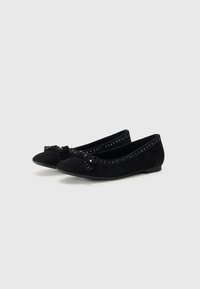 Ballet flats en daim noir avec un bout arrondi, un accent en nœud à l'avant et des clous décoratifs le long du bord. Semelle plate en caoutchouc.