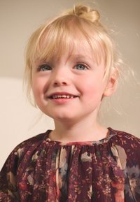 Vīnogu sarkana ziedu kleita ar plisētu izgriezumu un caurspīdīgu tekstūru, rotāta ar krāsainiem ziedu rakstiem uz tumša fona.