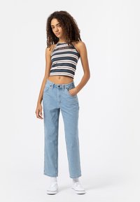 Pruhovaný halter crop top v námořnické modré, béžové a bílé, zkombinovaný se světle modrými džíny s vysokým pasem. Modelka má na sobě bílé tenisky.