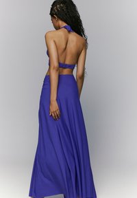 Conjunto de dos piezas en color púrpura que incluye un top halter con cuello atado y una falda maxi fluida. Textura suave con detalle de cinturilla fruncida.