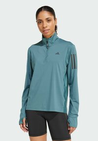 Teal long-sleeve sports shirt with half-zip collar. Features black three-stripe design on sleeves and moisture-wicking fabric.