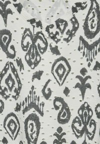 Tissu blanc avec des motifs gris complexes et une surface texturée comportant des trous découpés, créant un effet de design en couches.