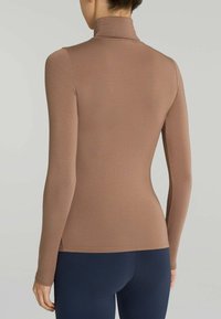 Maglietta a maniche lunghe, aderente, con colletto alto in un colore marrone tenue. Tessuto liscio con un colletto alto, realizzata in un tessuto elastico, abbinata a pantaloni blu navy.